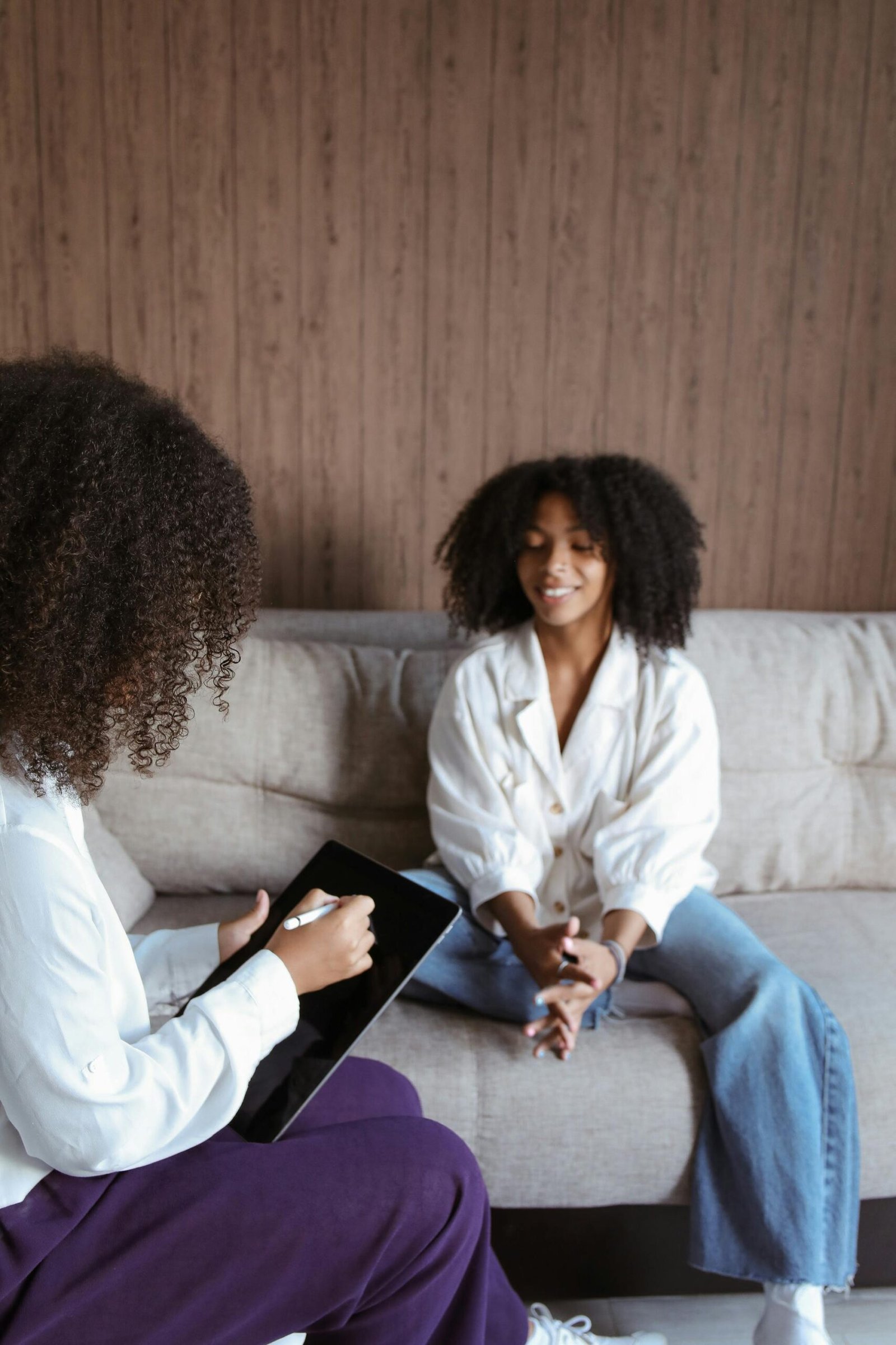 Two women discussing therapy while using a tablet in a cozy room.